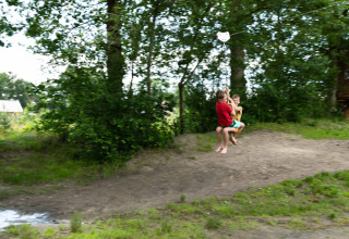 To børn leger på en svævebane i en skov omgivet af træer i ferieparken Beloofde Land, Gelderland.