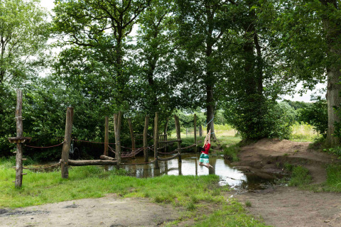 Kind schommelt aan een touw boven een vijver in het Beloofde Land vakantiepark, Gelderland.