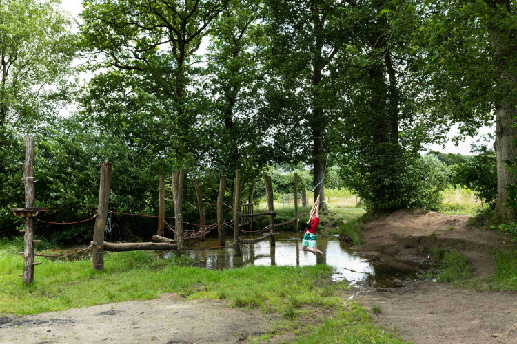 Kind schwingt an einem Seil über einen Teich auf einem Abenteuerspielplatz im Beloofde Land, Gelderland.