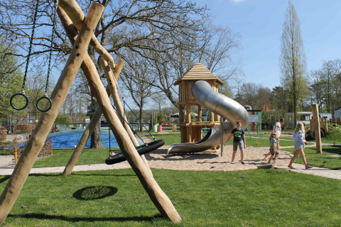 Kinder spielen auf einem Spielplatz mit Rutsche und Schaukeln im Ferienpark Beloofde Land, Gelderland.