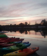 Kayaks alineados junto a un lago al atardecer en Camping de Kleine Wielen, parque vacacional en Frisia, Países Bajos.