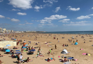 Zonnig strandtafereel aan Camping Paradis La Bretonniere in Pays de la Loire, Frankrijk, met veel vakantiegangers.