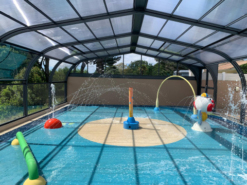 Überdachter Wasserspielplatz mit Spritzbrunnen und bunten Spielgeräten im Camping Paradis La Bretonnière, Frankreich.