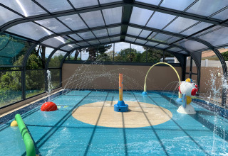 Überdachter Wasserspielplatz mit Spritzbrunnen und bunten Spielgeräten im Camping Paradis La Bretonnière, Frankreich.