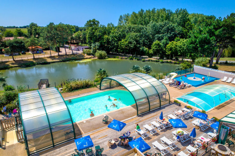 Piscinas al aire libre y tumbonas junto a un lago rodeado de árboles en Camping Paradis La Bretonniere, Pays de la Loire.