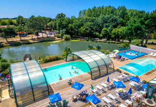 Udendørs swimmingpools og solsenge ved en sø omgivet af træer på Camping Paradis La Bretonniere, Pays de la Loire.
