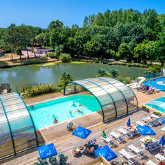 Piscinas al aire libre y tumbonas junto a un lago rodeado de árboles en Camping Paradis La Bretonniere, Pays de la Loire.
