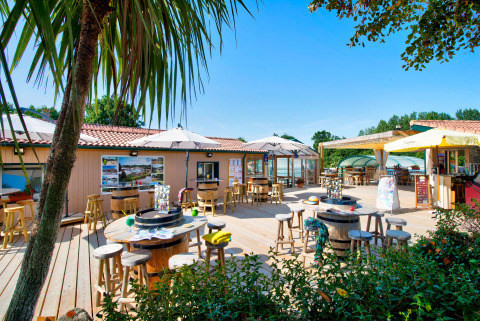 Terraza al aire libre con mesas y taburetes de madera en Camping Paradis La Bretonniere, Pays de la Loire, Francia.