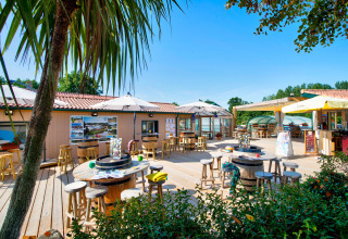 Sonnige Außenterrasse mit Holzstühlen und Sonnenschirmen im Camping Paradis La Bretonniere, Pays de la Loire.