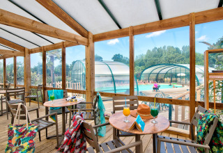 Überdachte Terrasse mit Tischen und Getränken, Blick auf das Hallenbad im Ferienpark in Pays de la Loire.