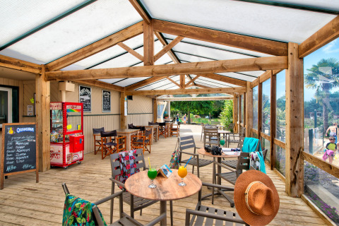 Terraza cubierta de madera con mesas y bebidas en Camping Paradis La Bretonniere en Pays de la Loire, Francia.