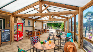 Terraza cubierta de madera con mesas y bebidas en Camping Paradis La Bretonniere en Pays de la Loire, Francia.