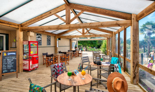 Terraza cubierta de madera con mesas y bebidas en Camping Paradis La Bretonniere en Pays de la Loire, Francia.