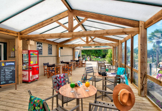 Überdachte Holzterrasse mit Sitzplätzen und Getränken im Camping Paradis La Bretonniere in Pays de la Loire, Frankreich.