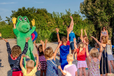 Niños juegan al aire libre con una persona disfrazada de rana en Camping Paradis La Bretonniere, Pays de la Loire, Francia.