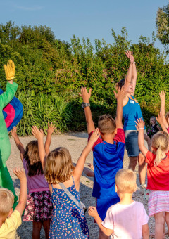 Niños juegan al aire libre con una persona disfrazada de rana en Camping Paradis La Bretonniere, Pays de la Loire, Francia.