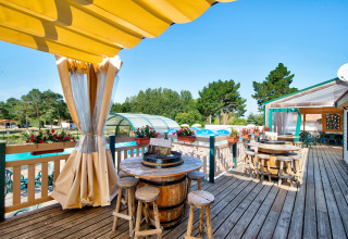 Sonnige Terrasse mit Fass-Tischen und Holzstühlen auf Camping Paradis La Bretonniere, Pays de la Loire, Frankreich.