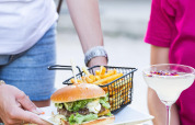 Servering af burger, pommes frites, cocktail og snacks udendørs på Camping le Mas de Mourgues i Occitanie.