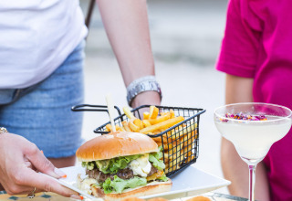 Servering af burger, pommes frites, cocktail og snacks udendørs på Camping le Mas de Mourgues i Occitanie.