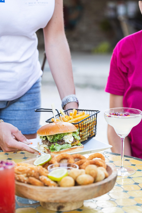 Hamburguesa, papas fritas, cóctel y aperitivos servidos al aire libre en Camping le Mas de Mourgues, Occitanie.