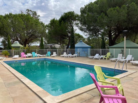 Piscina al aire libre con sillas coloridas y tumbonas en Camping le Mas de Mourgues, Occitania, Francia.