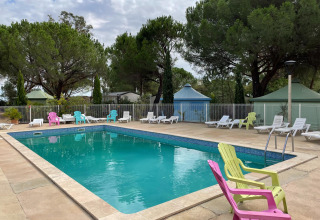 Udendørs swimmingpool med farverige stole og solvogne i Camping le Mas de Mourgues, Occitanie, Frankrig.