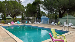 Außenpool mit bunten Stühlen und Sonnenliegen im Camping le Mas de Mourgues, Occitanie, Frankreich.