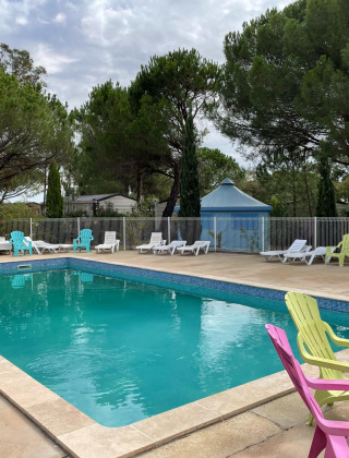 Piscina al aire libre con sillas coloridas y tumbonas en Camping le Mas de Mourgues, Occitania, Francia.