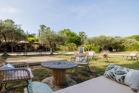 Zona de descanso al aire libre con muebles de mimbre y vegetación en Camping le Mas de Mourgues, Occitania, Francia.