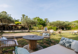 Zona de descanso al aire libre con muebles de mimbre y vegetación en Camping le Mas de Mourgues, Occitania, Francia.