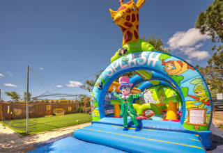 Inflatable playground with giraffe and clown mascot at Camping le Mas de Mourgues, Occitanie, France, sunny day.