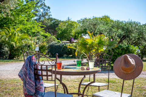 Mesa al aire libre con bebidas coloridas, sombrero de sol y bufanda en Camping le Mas de Mourgues, Occitania, Francia.