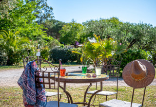 Mesa al aire libre con bebidas coloridas, sombrero de sol y bufanda en Camping le Mas de Mourgues, Occitania, Francia.