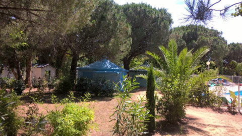 Camping le Mas de Mourgues en Occitania, Francia, rodeado de árboles, vegetación y una piscina soleada.