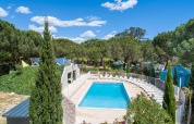 Udendørs swimmingpool med liggestole omgivet af træer på Camping le Mas de Mourgues i Occitanie, Frankrig.