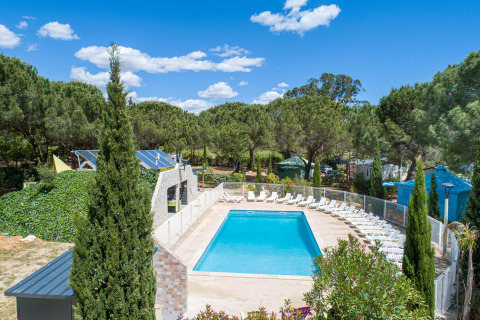 Outdoor swimming pool with lounge chairs surrounded by trees at Camping le Mas de Mourgues, Occitanie, France.