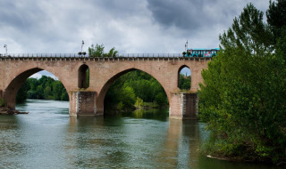 Alte Steinbogenbrücke mit Bus darüber, die einen ruhigen Fluss nahe Vauvert in der Region Okzitanien, Frankreich überspannt.