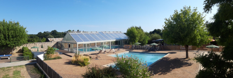 Piscina al aire libre y edificio acristalado rodeados de árboles en Huttopia Saumur, Pays de la Loire, Francia.