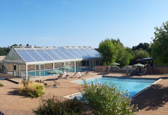 Piscina all'aperto e edificio di vetro circondati da alberi a Huttopia Saumur, Pays de la Loire, Francia.