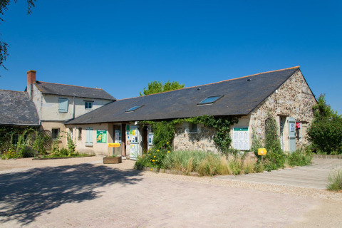 Edificio de recepción y casa de piedra bajo cielo azul en el Huttopia Saumur, Pays de la Loire, Francia.