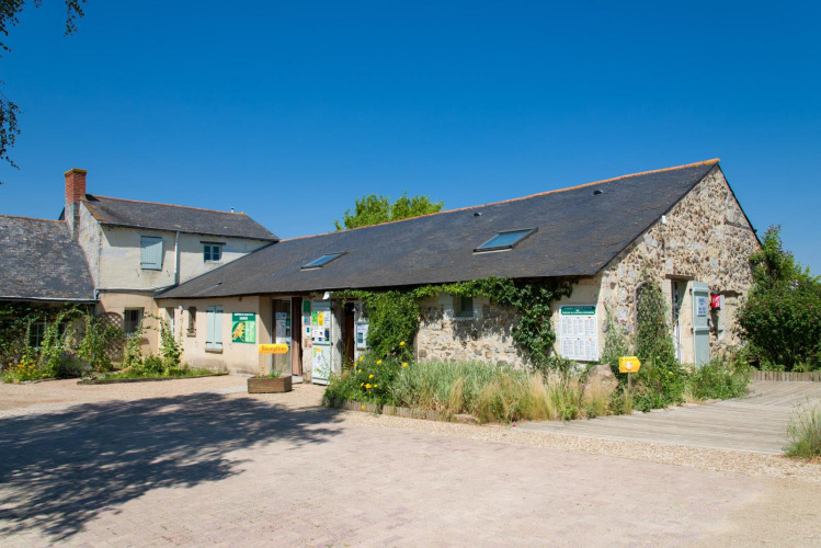 Reception building and stone house under clear blue sky at Huttopia Saumur holiday park, Pays de la Loire, France.