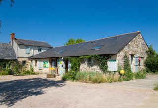 Edificio de recepción y casa de piedra bajo cielo azul en el Huttopia Saumur, Pays de la Loire, Francia.