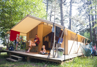Familie entspannt sich auf der Terrasse eines Safarizelts im Wald, umgeben von Bäumen und Natur.