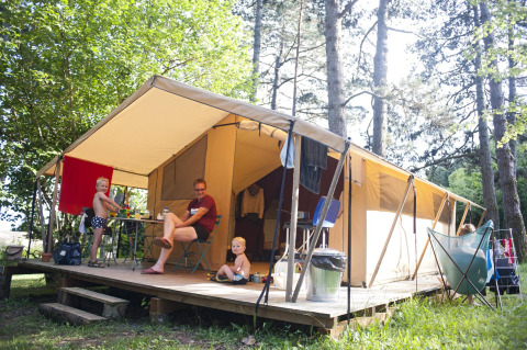 Family relaxing on the porch of a safari tent in the woods, children and adults enjoying the outdoors.
