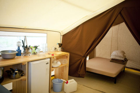 Vista interior de una tienda safari con cocina, nevera, utensilios y zona de dormitorio con cama.