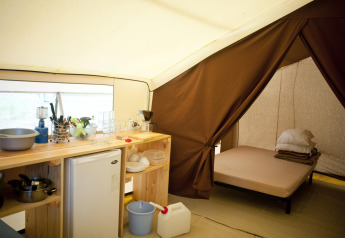 Innenansicht eines Safari-Zeltes mit Kochnische, Kühlschrank, Geschirr und einem Bett im Schlafbereich.
