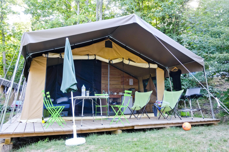 Safari tent Toile&Bois Sweet met houten terras, stoelen, tafel en barbecue in groene omgeving.