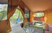 Vista interior de una tienda safari Toile&Bois tent Sweet con mesa, sillas y naturaleza exterior.