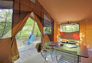 Vista interior de una tienda safari Toile&Bois tent Sweet con mesa, sillas y naturaleza exterior.