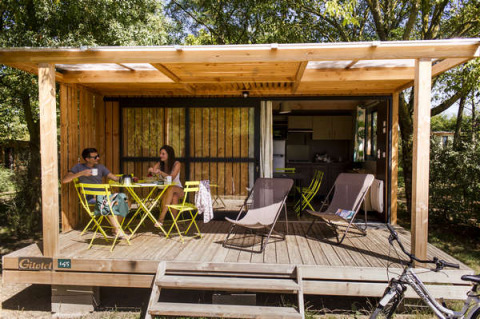 Dos personas relajándose y tomando algo en la terraza de madera del Chalet Evasion en Huttopia Saumur, Francia.